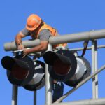 man in orange helmet climbing on white metal bar during daytime